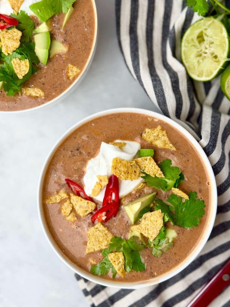 Close-up of creamy high-protein black bean soup topped with yogurt, avocado, cilantro, and crunchy tortilla chips.