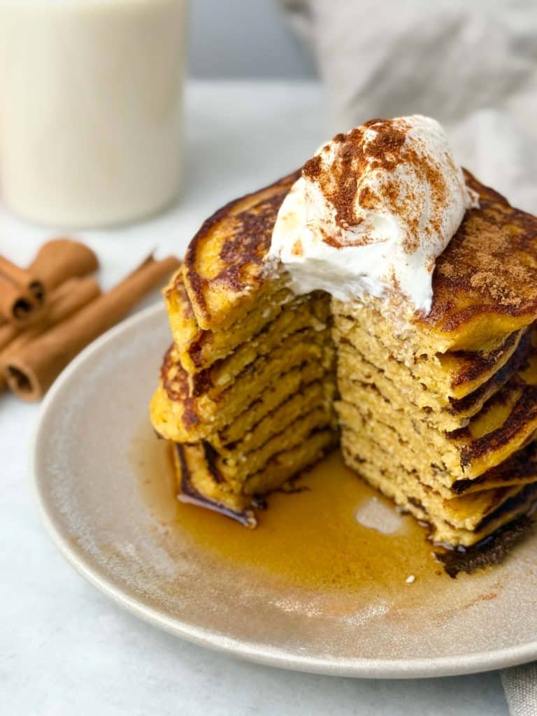 Stack of fluffy pumpkin protein pancakes topped with Greek yogurt and cinnamon.