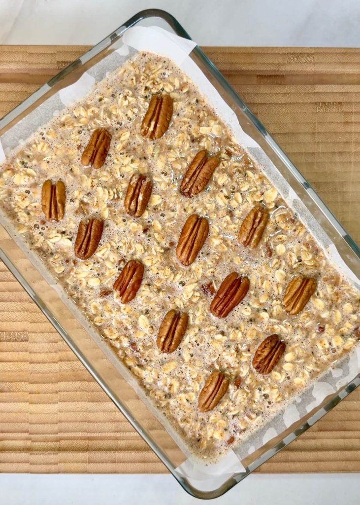 Unbaked pecan pie baked oatmeal mixture spread in a glass baking dish and topped with whole pecans before going into the oven.