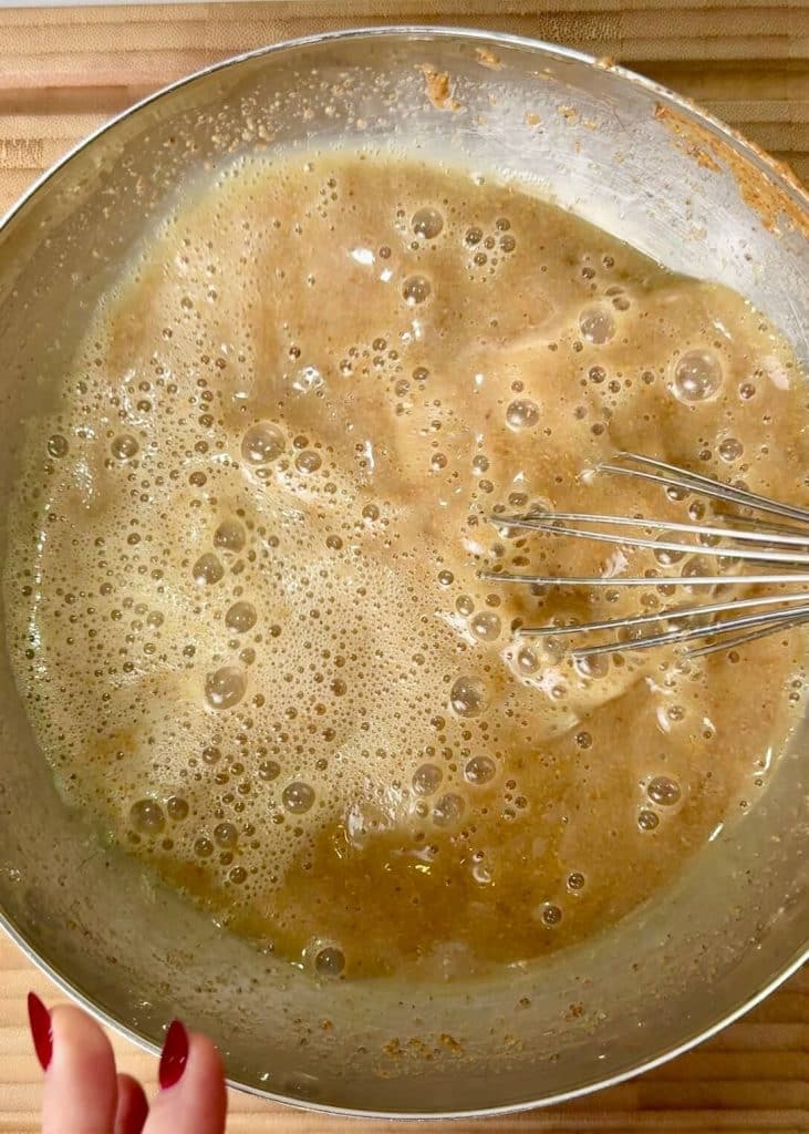 Wet ingredients for pecan pie baked oatmeal being whisked together in a bowl, including egg whites, maple syrup, almond butter, and vanilla.