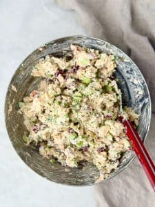 A stainless steel mixing bowl filled with creamy cranberry pecan chicken salad made with rotisserie chicken, celery, dried cranberries, dill, and toasted pecans, ready to serve.
