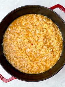 Orzo simmering in chicken bone broth with sautéed onions to create a creamy one-pot lemon chicken orzo.
