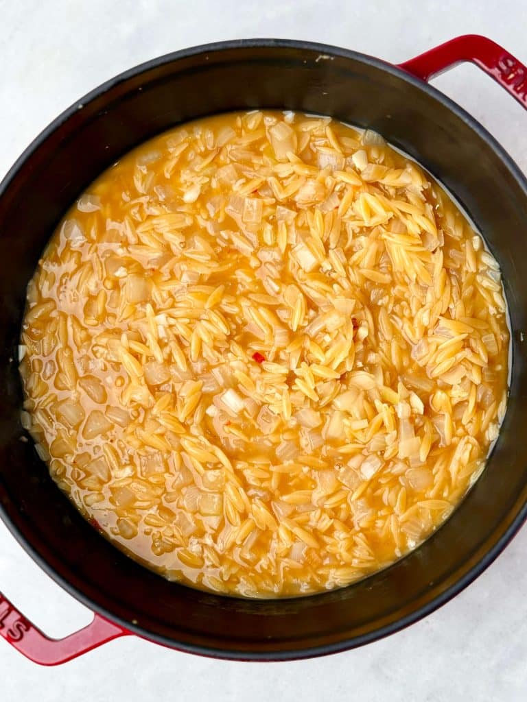 Orzo simmering in chicken bone broth with sautéed onions to create a creamy one-pot lemon chicken orzo.