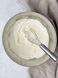 A bowl of creamy Greek yogurt and mayo dressing whisked until smooth, the base for a healthy cranberry pecan chicken salad.