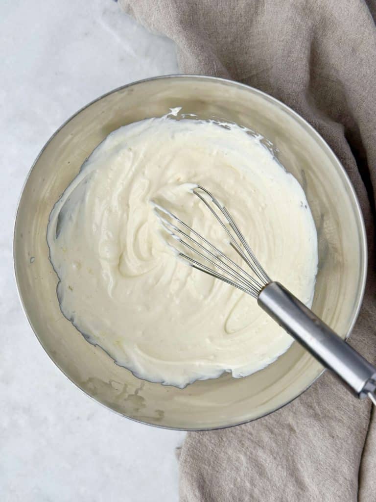 A bowl of creamy Greek yogurt and mayo dressing whisked until smooth, the base for a healthy cranberry pecan chicken salad.