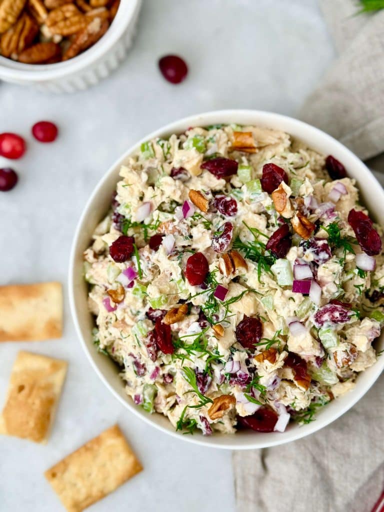 Overhead shot of cranberry pecan chicken salad in a bowl with visible celery, dried cranberries, pecans, red onion, and herbs for texture and color.