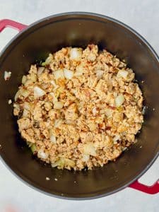 Chicken sausage, onions, garlic, and chili flakes sautéing in a Dutch oven as the flavor base for creamy white lasagna soup.