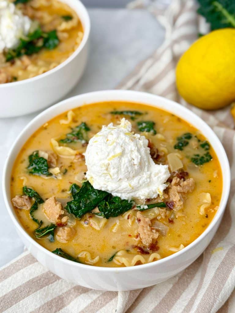 Creamy white lasagna soup in a bowl topped with lemon ricotta and Tuscan kale, made with chicken sausage and broken lasagna noodles.