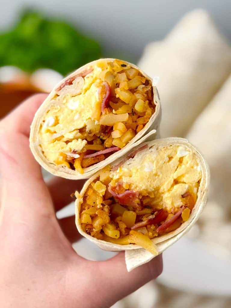 Close-up of a halved freezer breakfast burrito filled with scrambled eggs, crispy hash browns, and bacon.