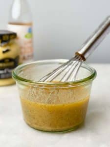 Brown butter Dijon vinaigrette in a glass jar with a whisk, ready for the harvest quinoa salad.