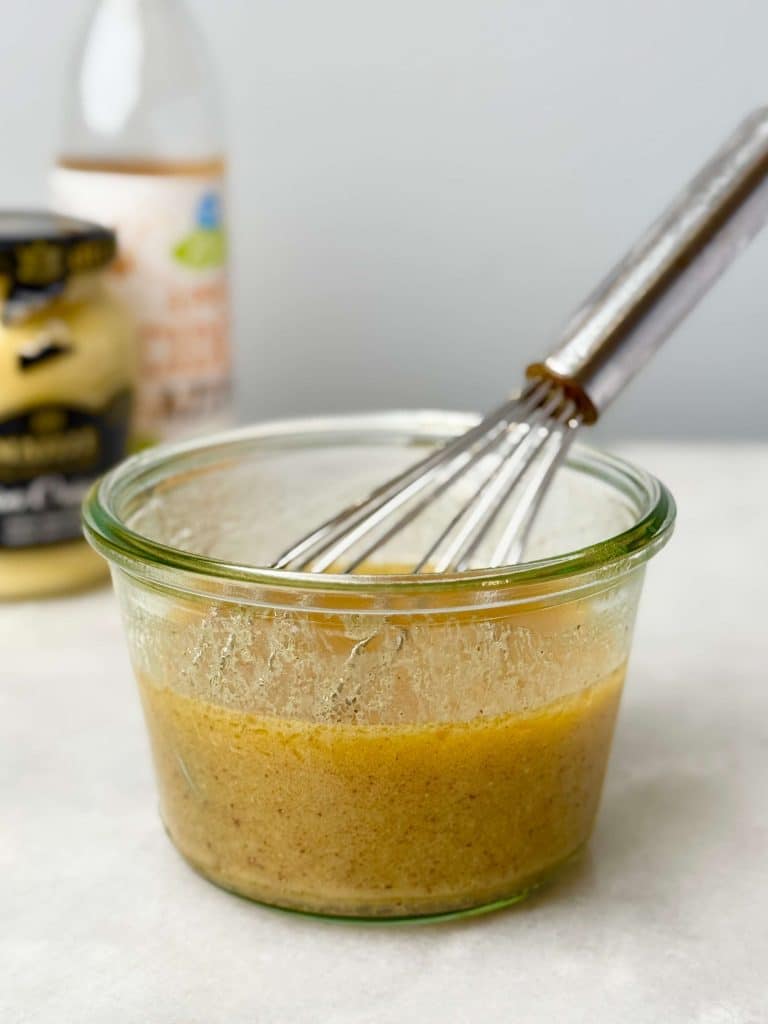 Brown butter Dijon vinaigrette in a glass jar with a whisk, ready for the harvest quinoa salad.