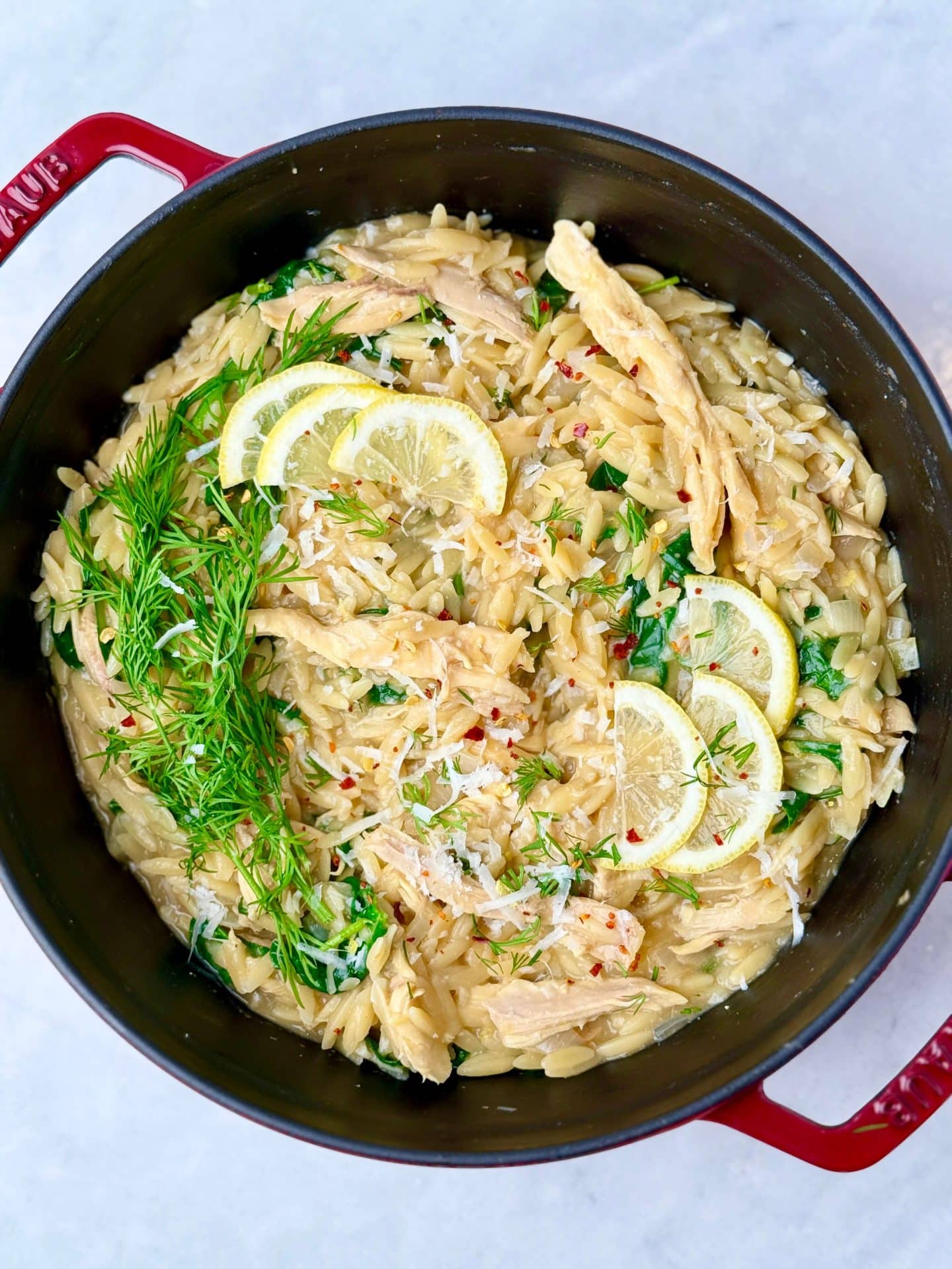 Creamy lemon chicken orzo finished with parmesan, fresh dill, and lemon slices in a red Dutch oven.