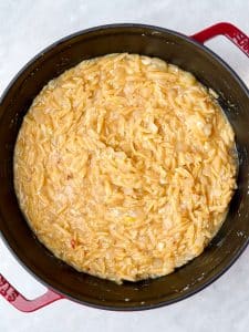 Creamy orzo cooking down in broth before adding chicken, parmesan, lemon, and spinach.