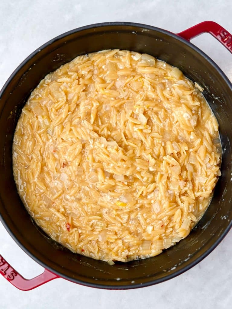Creamy orzo cooking down in broth before adding chicken, parmesan, lemon, and spinach.