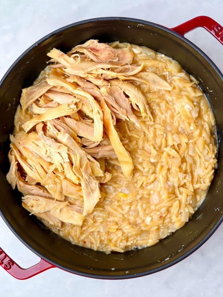 Shredded rotisserie chicken being folded into creamy orzo for an easy one-pot lemon chicken orzo recipe.
