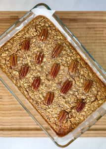 Fully baked pecan pie baked oatmeal in a glass dish, topped with whole pecans and golden edges, ready to slice into breakfast squares.