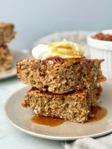 Two slices of pecan pie baked oatmeal stacked on a plate and topped with yogurt and maple syrup for a cozy, high-protein breakfast.