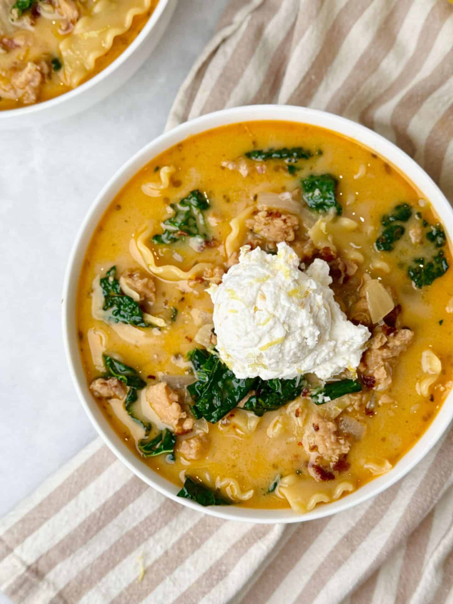Overhead view of creamy white lasagna soup with chicken sausage, kale, and lasagna noodles, finished with a dollop of lemon ricotta.