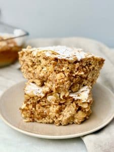 Stacked almond croissant baked oatmeal squares dusted with powdered sugar and sliced almonds, served on a plate.