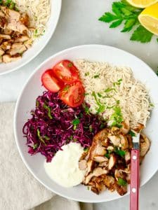 Air fryer chicken shawarma bowl with rice, shredded red cabbage salad, garlicky yogurt sauce, and sliced tomatoes.