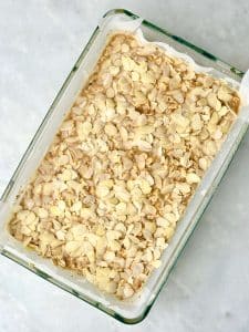 Almond croissant baked oatmeal before baking, topped with sliced almonds in a parchment-lined glass baking dish.