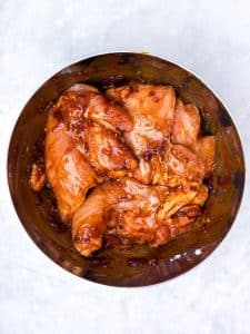 Chicken breasts tossed in BBQ marinade in a stainless steel mixing bowl