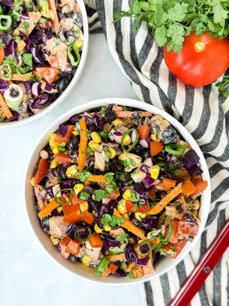 Two bowls of BBQ chicken dense bean salad on a striped linen with tomato and cilantro