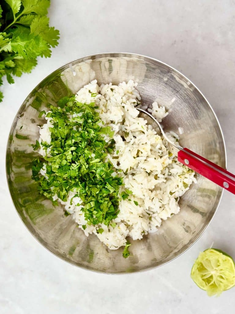 Cilantro lime rice mixed in a bowl with fresh herbs and lime juice for a copycat Chipotle burrito bowl.