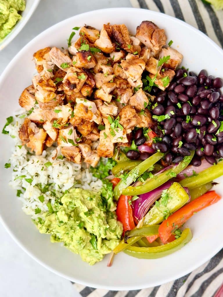 Close-up of a copycat Chipotle burrito bowl featuring chopped chipotle chicken thighs, cilantro lime rice, and fajita veggies.