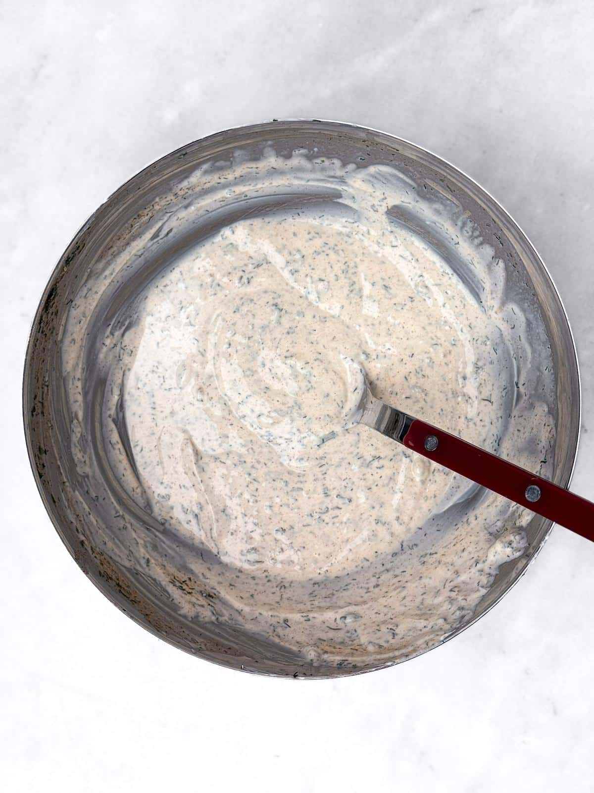 Creamy herb yogurt dressing in a metal bowl with a red spatula