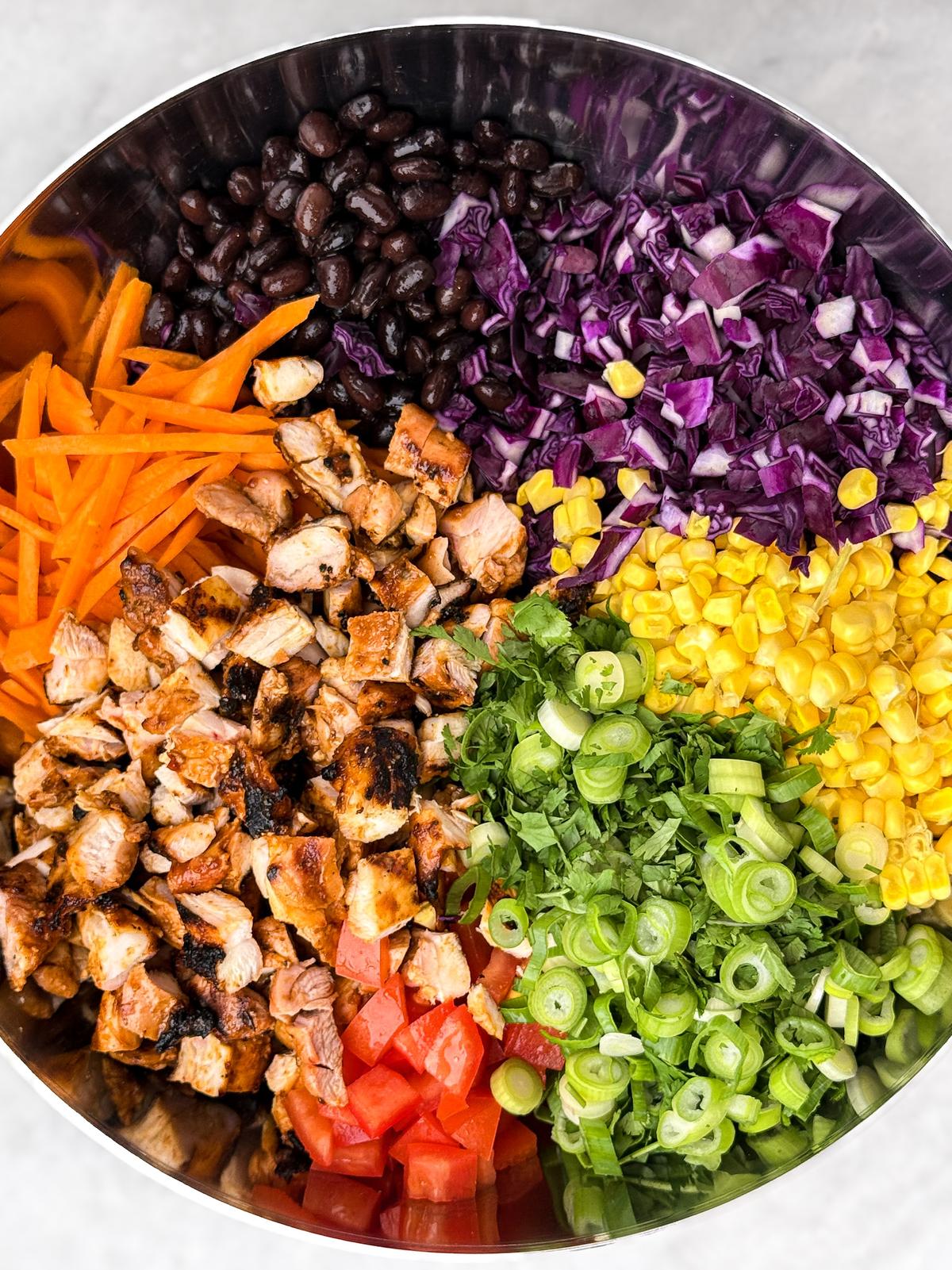 Black beans, red cabbage, corn, carrots, tomato, and chopped chicken arranged in a bowl