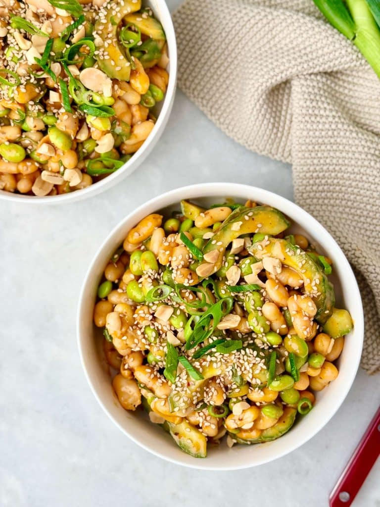 Dense bean salad with edamame, white beans, cucumber, green onions, and sesame seeds coated in miso peanut dressing.