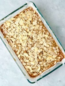 Freshly baked almond croissant baked oatmeal with golden edges and sliced almonds on top, ready to slice for meal prep.