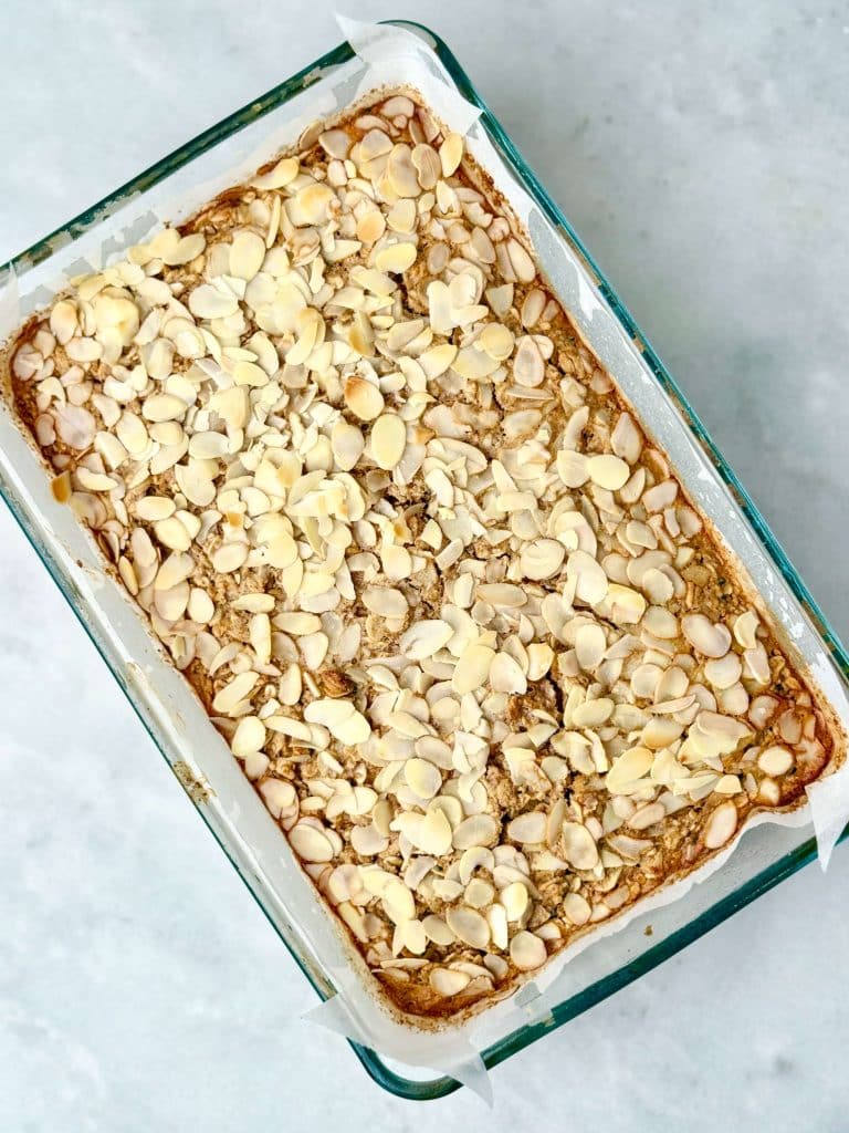 Freshly baked almond croissant baked oatmeal with golden edges and sliced almonds on top, ready to slice for meal prep.