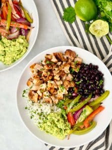 Homemade copycat Chipotle burrito bowl served with chicken, peppers and onions, black beans, rice, and fresh guacamole.