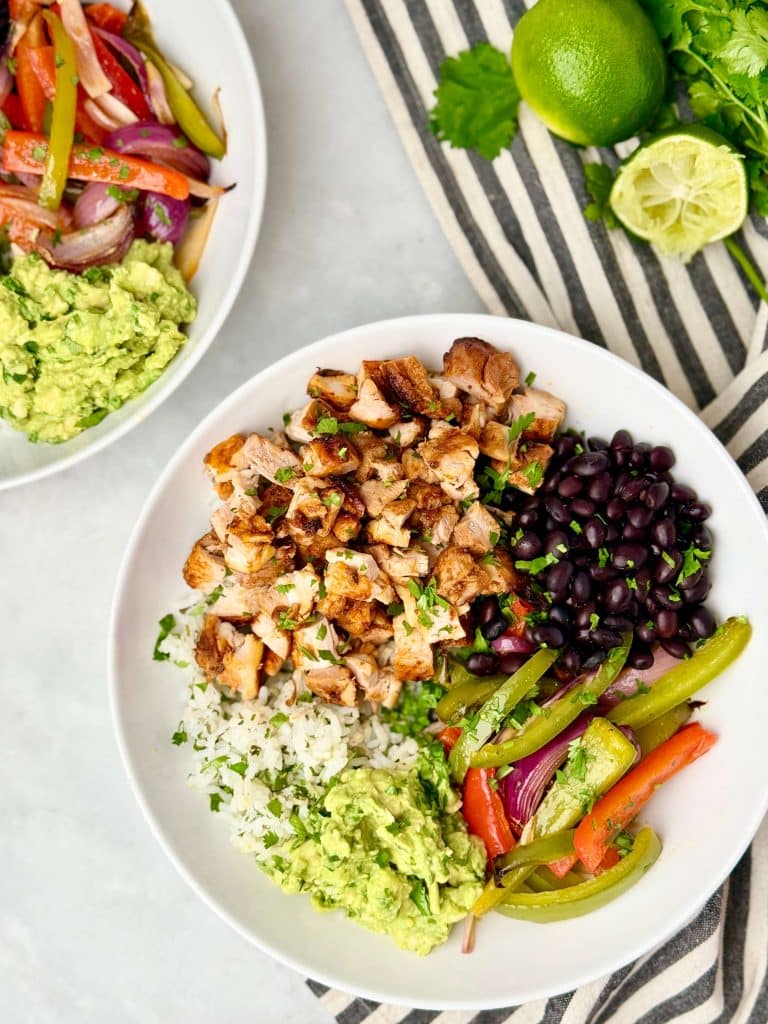 Homemade copycat Chipotle burrito bowl served with chicken, peppers and onions, black beans, rice, and fresh guacamole.