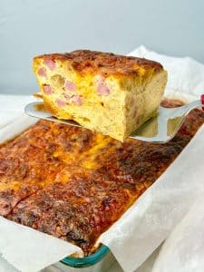 Slice of high protein breakfast casserole lifted from the baking dish, showing a soft, custardy egg interior.