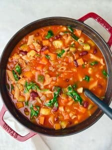 High protein minestrone soup simmering in a Dutch oven with pasta, beans, and vegetables