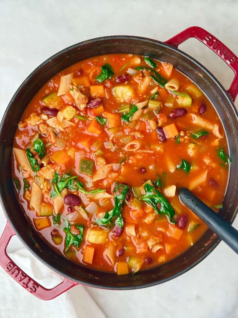 High protein minestrone soup simmering in a Dutch oven with pasta, beans, and vegetables