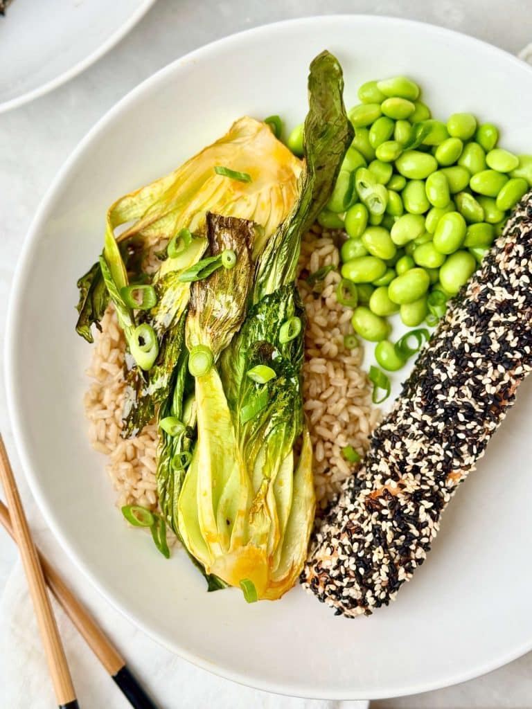 Sesame crusted salmon bowl with rice, edamame, and roasted bok choy in a white bowl