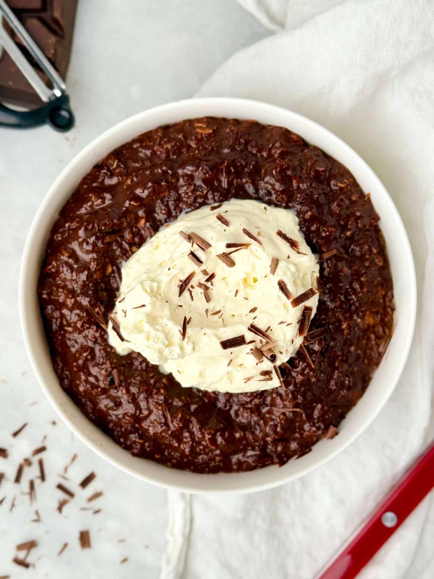 Hot chocolate protein oats topped with whipped cream and chocolate shavings in a white bowl
