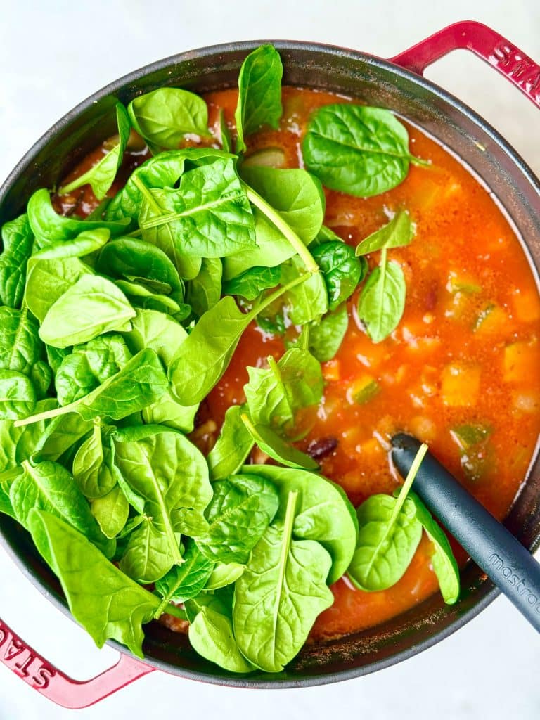 Fresh spinach added to high protein minestrone soup during the final cooking step