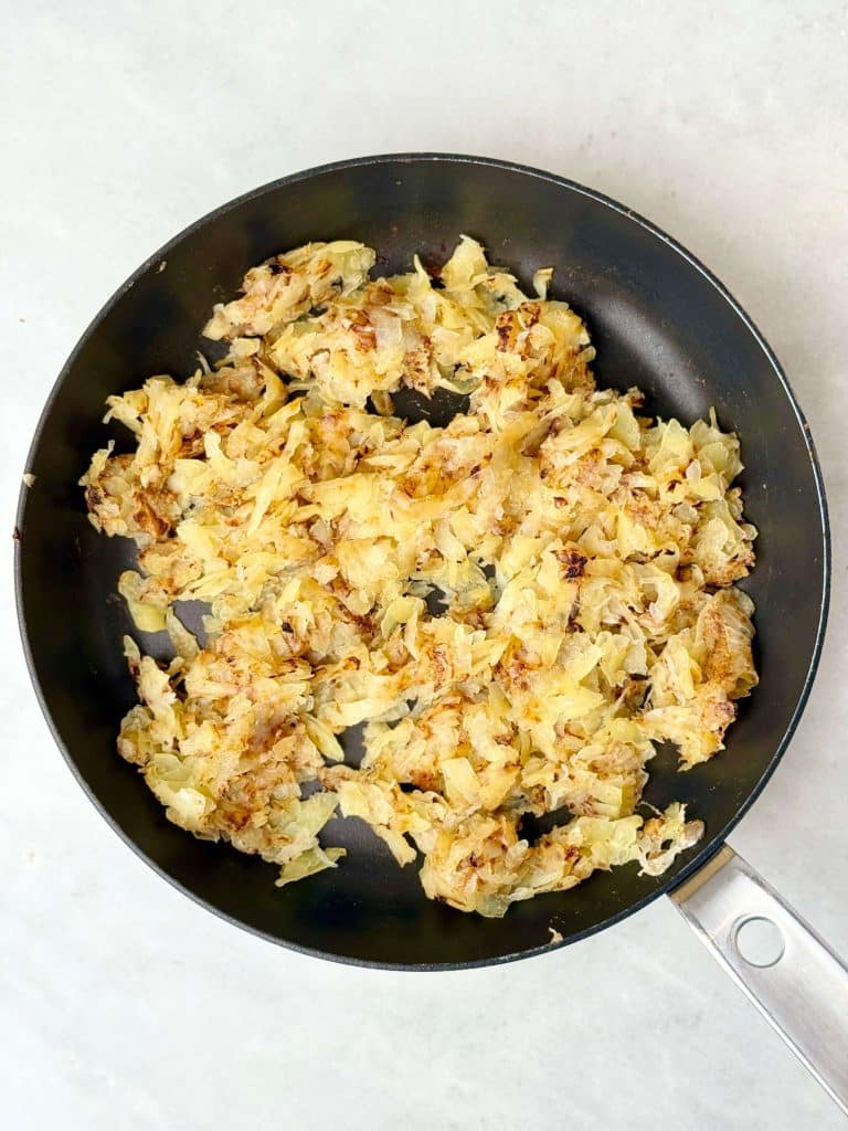Grated potato and onion sautéed in a skillet as the base for a protein-packed breakfast casserole with eggs and ham.