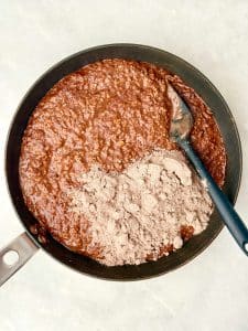 Adding chocolate protein powder to hot chocolate protein oats while cooking on the stovetop