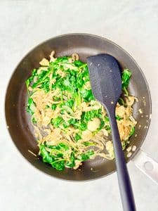 Spinach and onion sautéed in a skillet for a high-protein spanakopita wrap filling