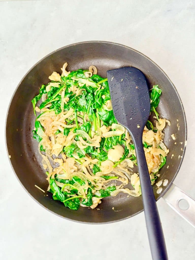 Spinach and onion sautéed in a skillet for a high-protein spanakopita wrap filling