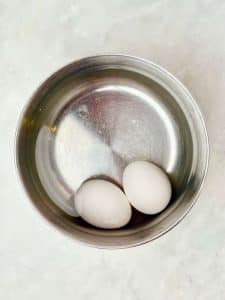 Two eggs in a saucepan before boiling, an easy first step for making jammy eggs for a high protein snack plate.