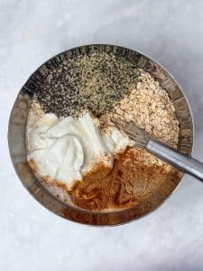 Rolled oats, chia seeds, hemp hearts, Greek yogurt, and chai spices ready to be mixed into overnight oats.