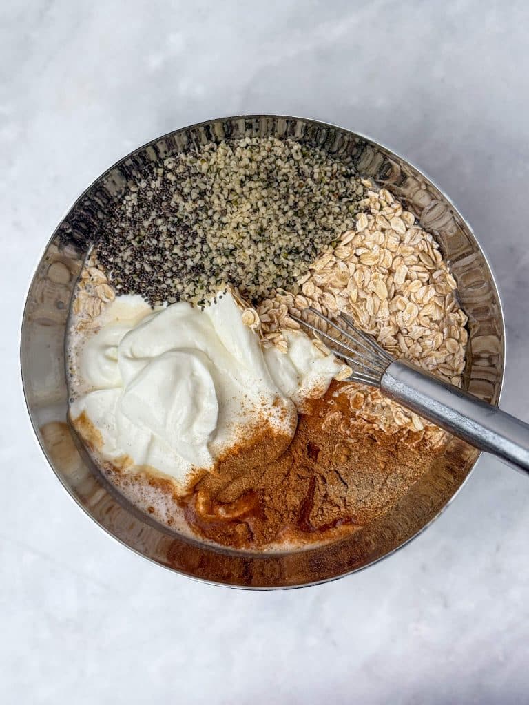 Rolled oats, chia seeds, hemp hearts, Greek yogurt, and chai spices ready to be mixed into overnight oats.