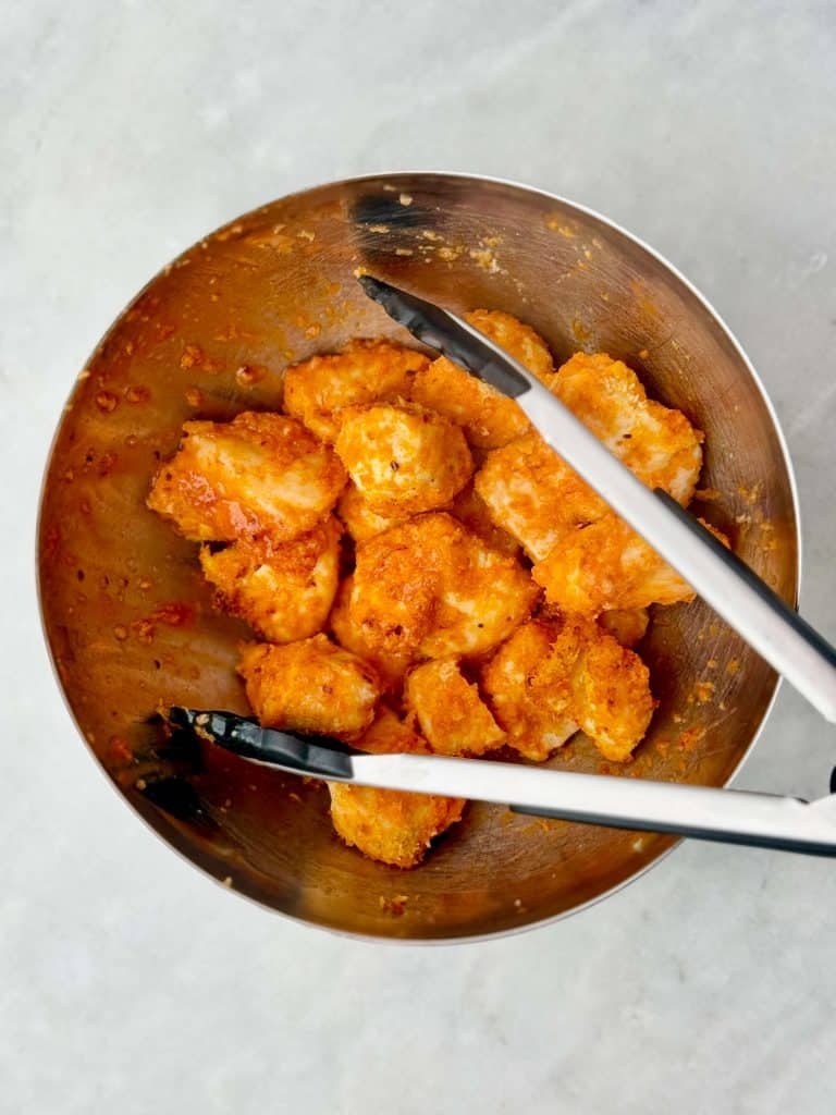 Crispy air fryer buffalo chicken bites being tossed in buffalo sauce in a mixing bowl.